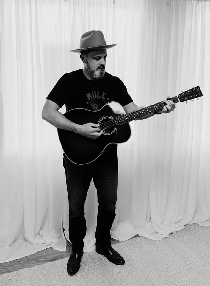 Person standing and playing an acoustic guitar.