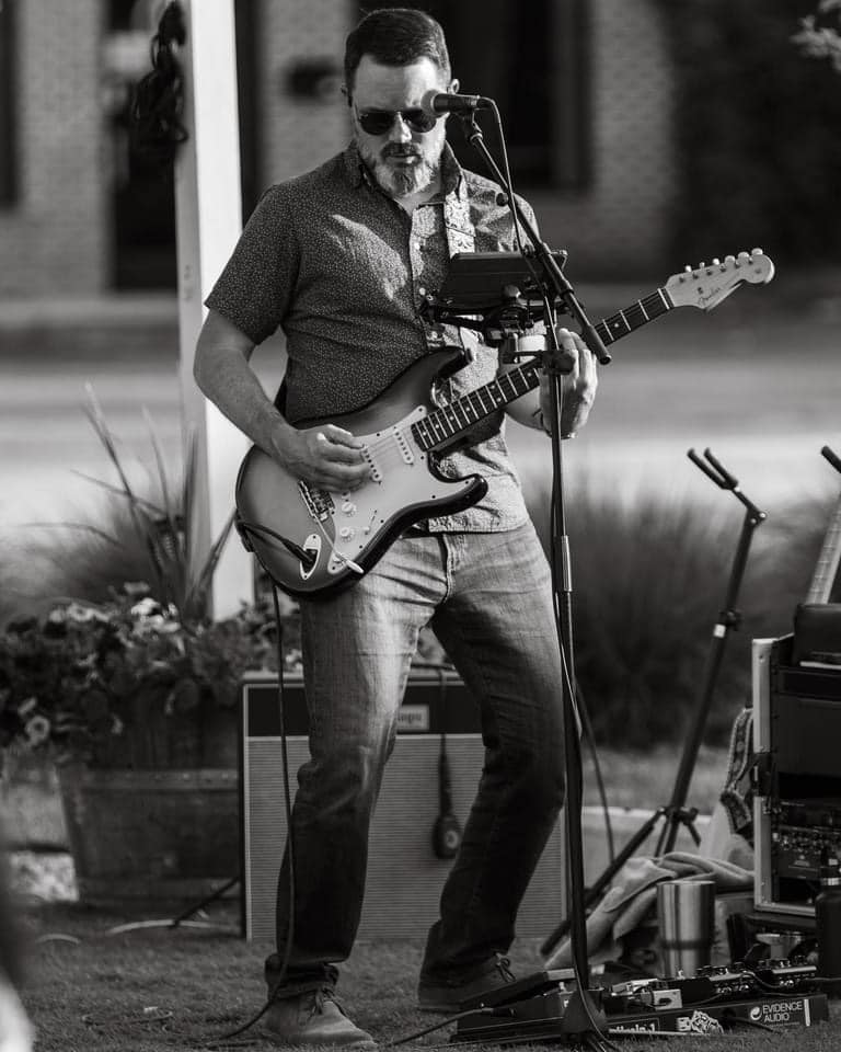 Person standing outside playing electric guitar.